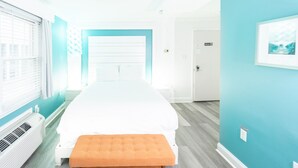 A hotel room with a large bed, a bench, a window with blinds, and a door.