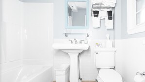 A modern bathroom with a bathtub, a pedestal sink, a toilet, and a mirror.