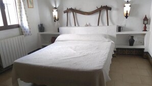 Un dormitorio con cabecera de madera, dos mesitas de noche, un radiador y una ventana con cortinas.