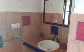 Un baño con un lavabo blanco, un espejo y una pared con baldosas en tonos rosa y azul.