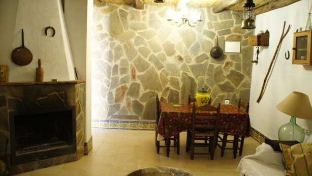Un comedor con paredes de piedra, una mesa dispuesta para dos personas, una chimenea y una lámpara.