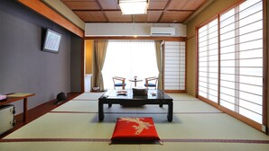 A traditional Japanese room with tatami flooring, a low table with cushions, sliding doors, and a ceiling fan. - Raki Onsenryokan (Yamanouchi)