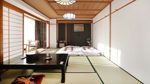 A traditional Japanese room with tatami flooring, a low table with a remote control, and a bed with a white blanket. - Raki Onsenryokan (Yamanouchi)