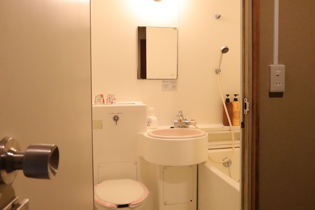 A small, well-lit bathroom with a toilet, sink, and shower.