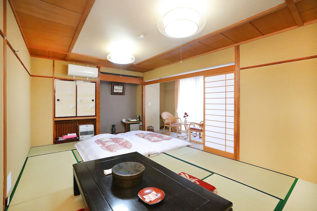 A traditional Japanese room with tatami flooring, a bed with white bedding, a wooden table with a bowl, and sliding doors.