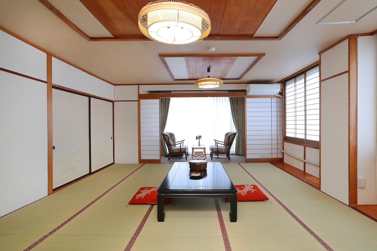 A traditional Japanese room with tatami flooring, a low table with a decorative item, and sliding doors.