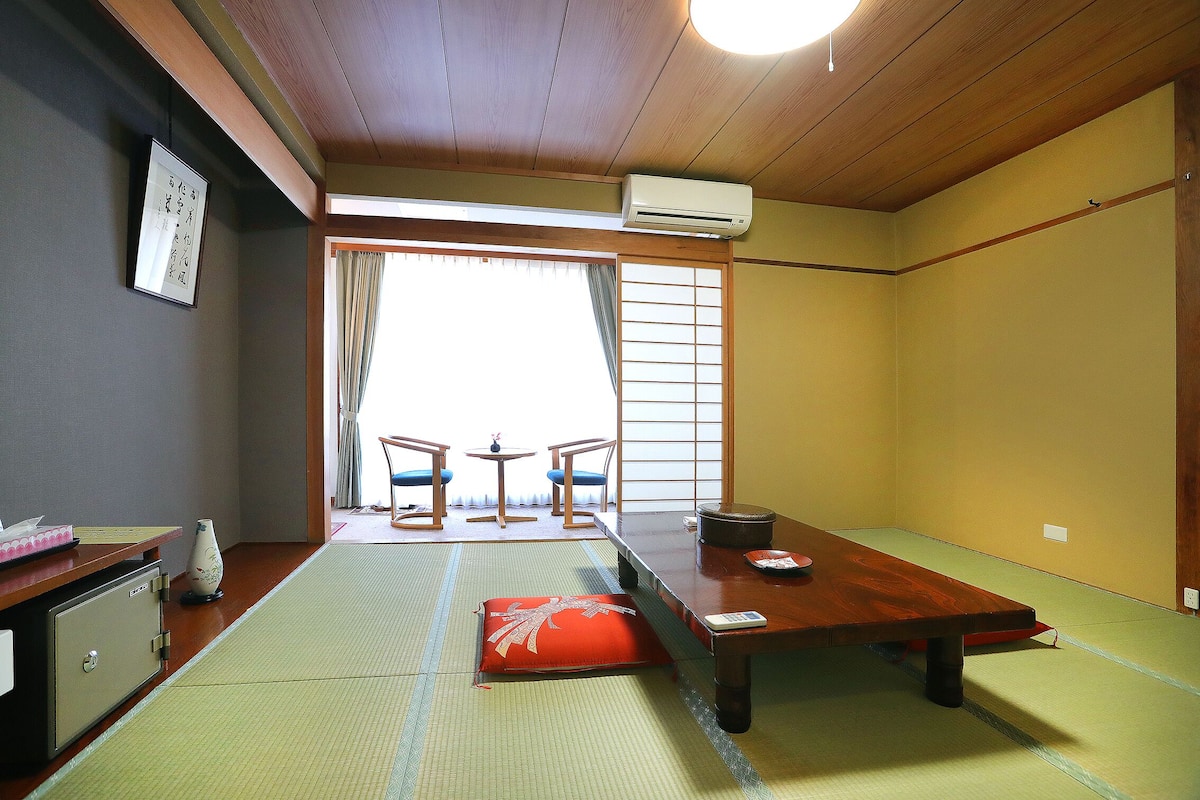 A traditional Japanese room with tatami flooring, a low table, and a sliding door leading to a balcony.