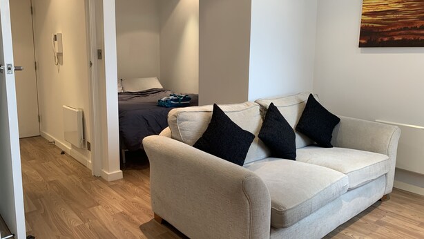 A modern living room with a beige sofa, black cushions, and a painting on the wall. - StayHere 3 (Leeds)