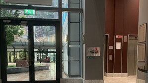 A lobby with a glass entrance, a bench, and an elevator area. - StayHere 3 (Leeds)