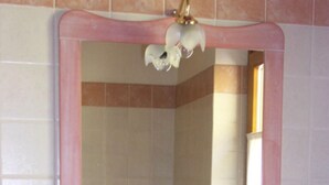 Een badkamer met een spiegel met roze lijst, een witte wastafel en een lamp boven de spiegel.