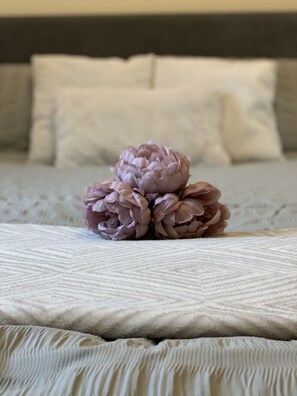 A bed with a textured white cover, a dark headboard, and a single decorative flower arrangement.