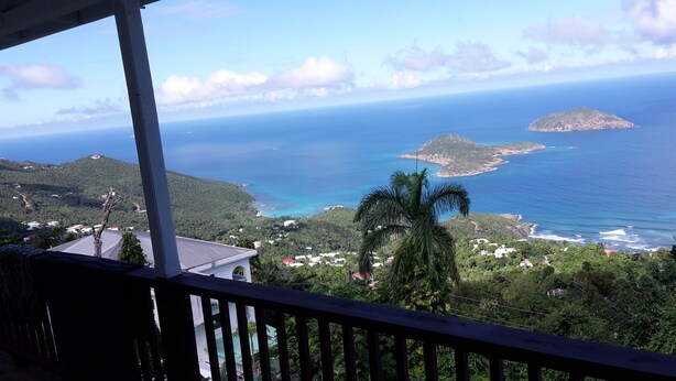 Blick aufs Meer vom Balkon mit Holzgeländer, mit Blick auf ein türkisblaues Meer, grüne Hügel und eine kleine Insel.