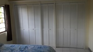 Ein Schlafzimmer mit einem Bett, einem Fenster mit Vorhängen und mehreren weißen Schränken.