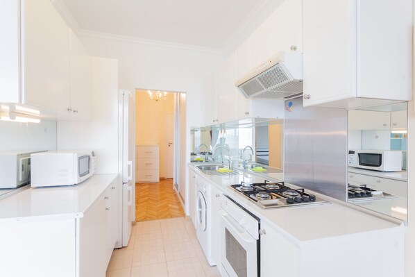 A modern kitchen with white cabinets, a stainless steel range hood, a microwave, and a washing machine.