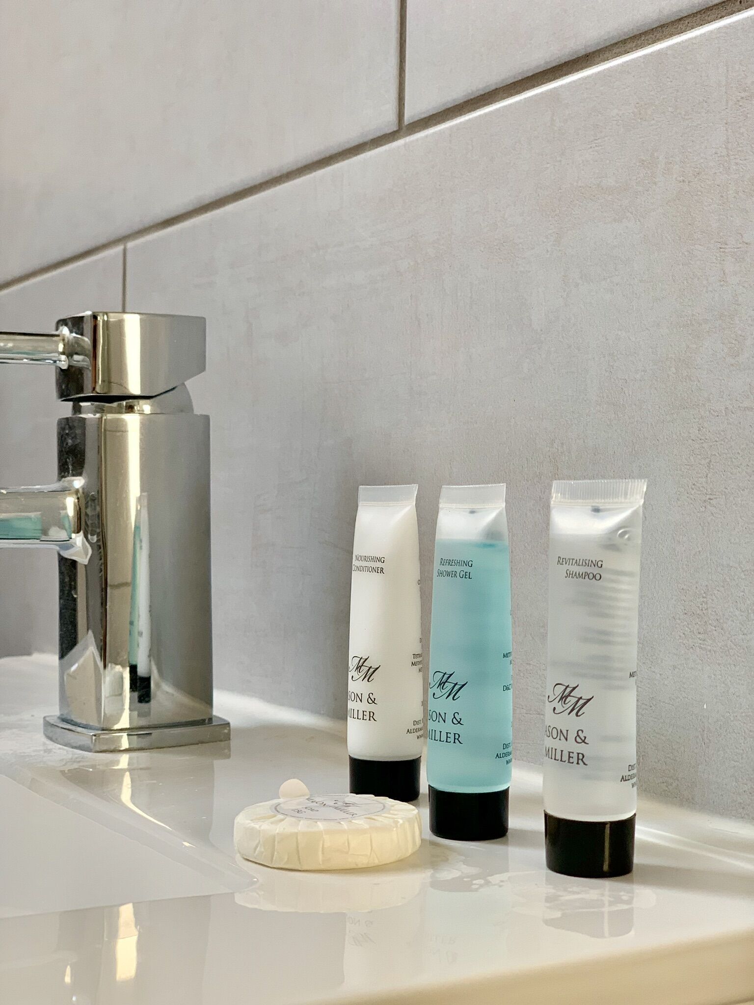 Une salle de bain équipée d’un robinet moderne, de trois produits de toilette (après-shampoing, gel douche, shampoing) et d’un porte-savon.