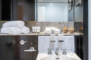 Une salle de bain moderne avec un lavabo en marbre, deux robinets et un miroir. On y trouve des serviettes et des articles de toilette sur le comptoir.
