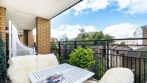 En balkon med et hvidt bord, en blød hvid stol og en lille potteplante.