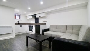 A modern living room with a grey sofa, a black coffee table, and a kitchen area in the background. - StayHere 6 (Leeds)