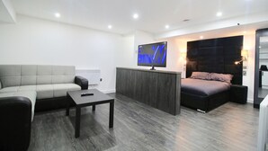 A modern living room with a sofa, a coffee table, a TV mounted on a wall, and a bed with a headboard. - StayHere 6 (Leeds)