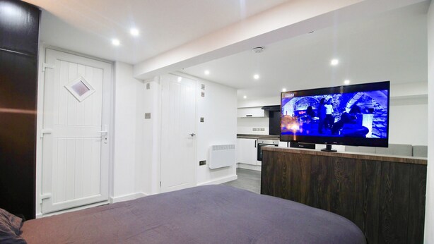 A bedroom with a bed, a TV, a wooden dresser, and a white door. - StayHere 6 (Leeds)