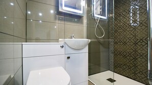 A modern bathroom with a white toilet, a sink, and a glass shower enclosure. - StayHere 6 (Leeds)