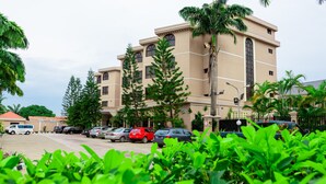 Ein mehrgeschossiges Hotel mit einer beige farbenen Fassade, geparkten Autos und üppiger Bepflanzung im Vordergrund.