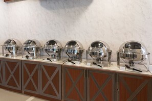 A buffet setup with multiple food dispensers on a counter, each with a dome cover and labeled with utensils. - Regenta Central Residency (Pattaya)