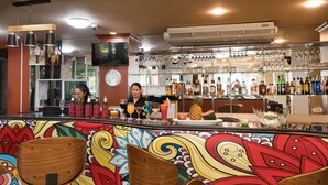 A bar area with a colorful mural, wooden chairs, and a variety of bottles and glasses on shelves. - Regenta Central Residency (Pattaya)