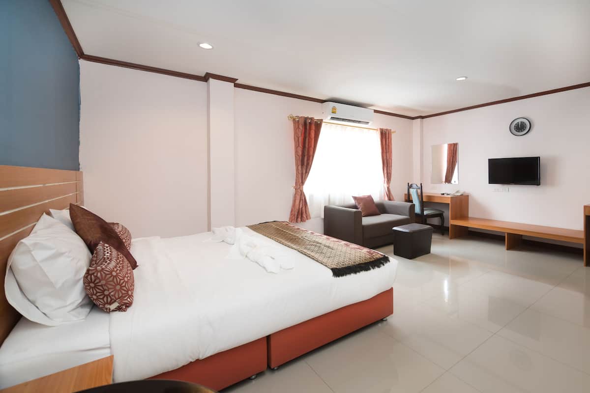 Quarto de hotel com cama grande, escrivaninha, cadeira, televisão e janela com cortinas.