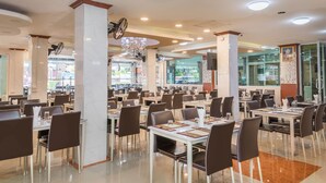A spacious restaurant with multiple dining tables and chairs, large windows, and a chandelier. - Regenta Central Residency (Pattaya)