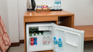A compact refrigerator with a wooden countertop above it, containing a kettle, snacks, and bottled water. - Regenta Central Residency (Pattaya)