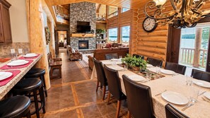 A log cabin interior with a dining area, kitchen, and fireplace. - Waters Edge* 9Br+loft, 5.5Ba, Boat Dock, Wifi (Island Park)