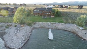 A large house with a river in front, surrounded by open fields and other houses. - Waters Edge* 9Br+loft, 5.5Ba, Boat Dock, Wifi (Island Park)