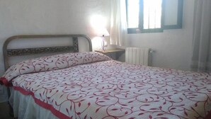 Ein Schlafzimmer mit Bett, Nachttisch, Lampe, einem Fenster mit Vorhängen und einer Heizung.
