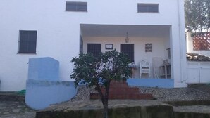 Ein weißes Gebäude mit einer kleinen Veranda, einem Baum davor und einer blauen Wand.