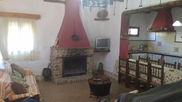 Ein gemütliches Wohnzimmer mit Kamin aus Stein, einem Fernseher und einem Essbereich mit Holztisch und Stühlen.