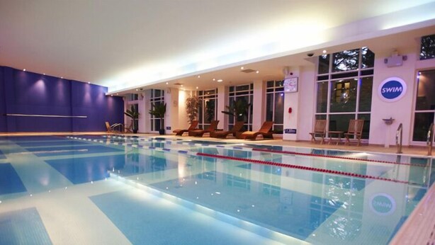 An indoor swimming pool with clear lane dividers, lounge chairs, and a 'SWIM' sign on the wall. - The Lodge at Meyrick Park (Bournemouth)