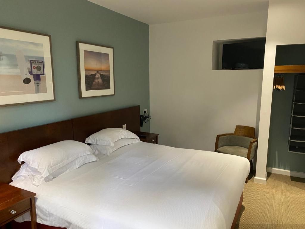 A hotel room with a large bed, a nightstand, a chair, a television mounted on the wall, and framed pictures on the wall.