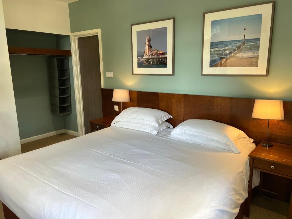 Une chambre d’hôtel avec un grand lit, deux lampes de chevet, une tête de lit en bois et deux tableaux encadrés au mur.
