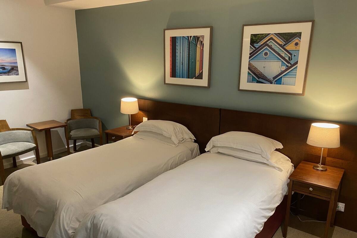 A hotel room with two beds, two nightstands, a chair, and two framed pictures on the wall.