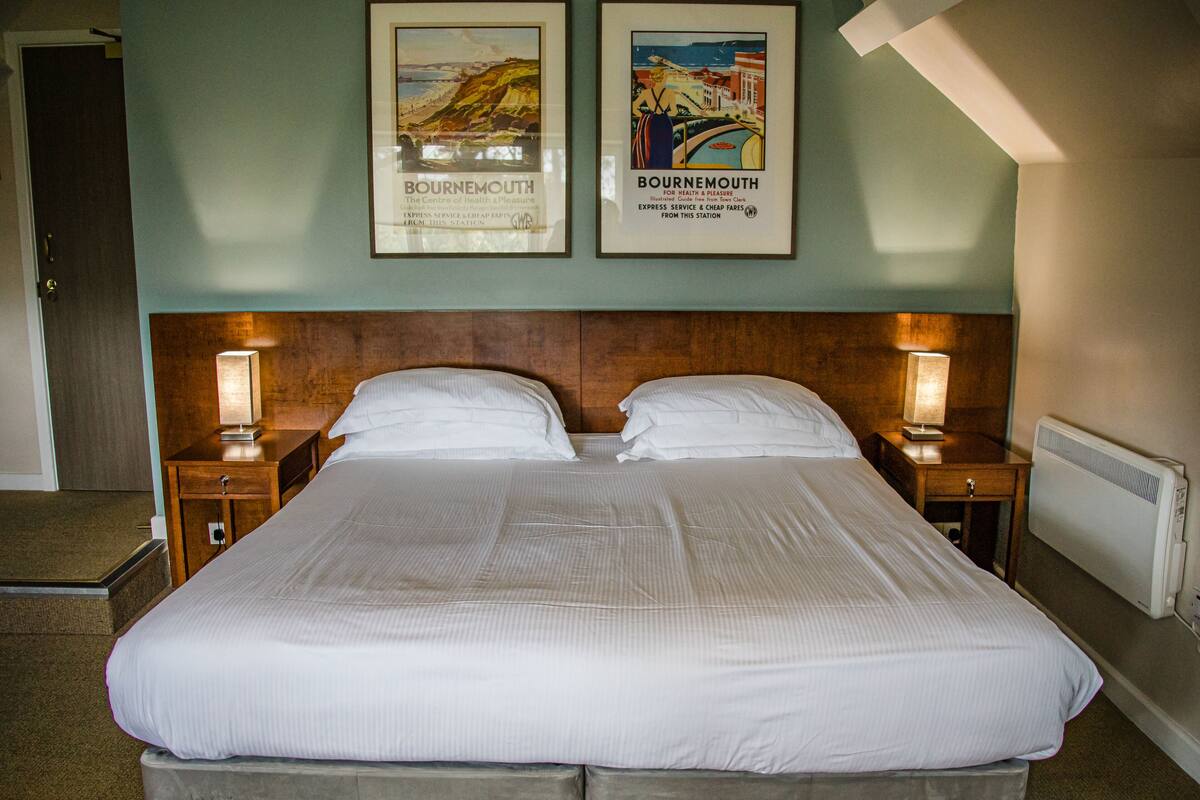 A hotel room with a large bed, two bedside tables with lamps, and two framed posters on the wall.