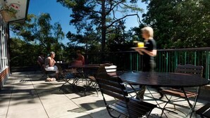 An outdoor patio with metal tables and benches, surrounded by a brick wall and trees. - The Lodge at Meyrick Park (Bournemouth)