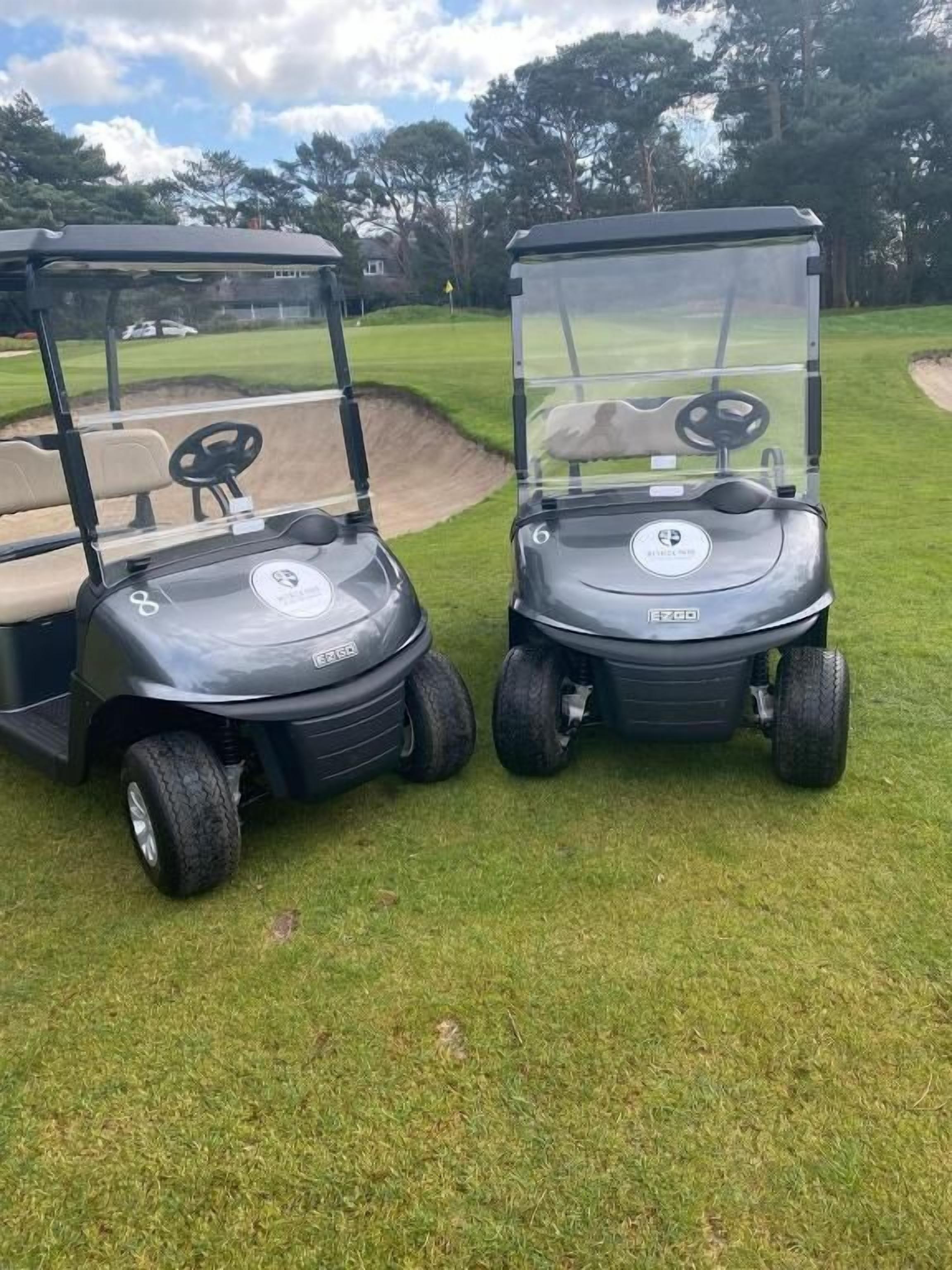 Two golf carts on a grassy field with a clear sky.