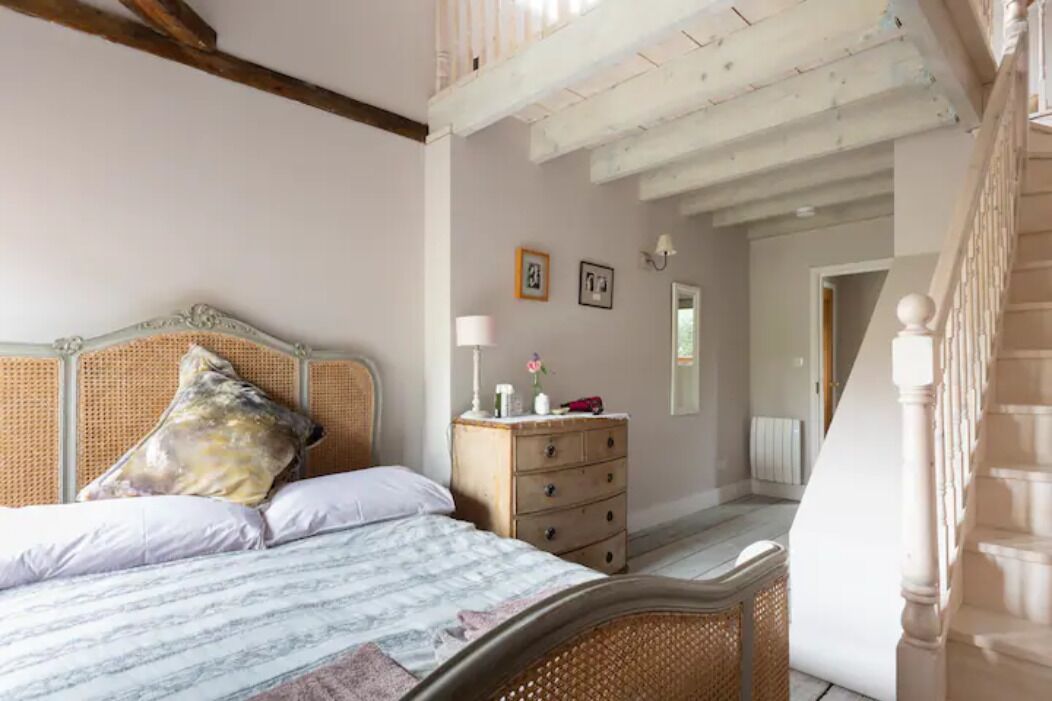 A bedroom with a bed, a dresser, and a staircase.