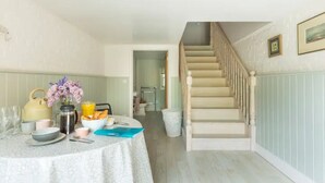 Ein Essbereich mit einem runden Tisch, gedeckt für das Frühstück, einer Treppe und Blick in einen anderen Raum.