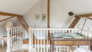 Ein Zimmer mit Holzbalkendecke, weißen Geländern, einem Schreibtisch mit Zeitschriften und gerahmten Bildern an der Wand.
