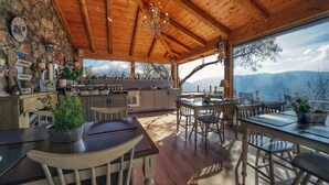 Une vaste salle à manger en bois offrant une vue sur les montagnes, un mur en pierre orné d’horloges et une cuisine avec vue panoramique.