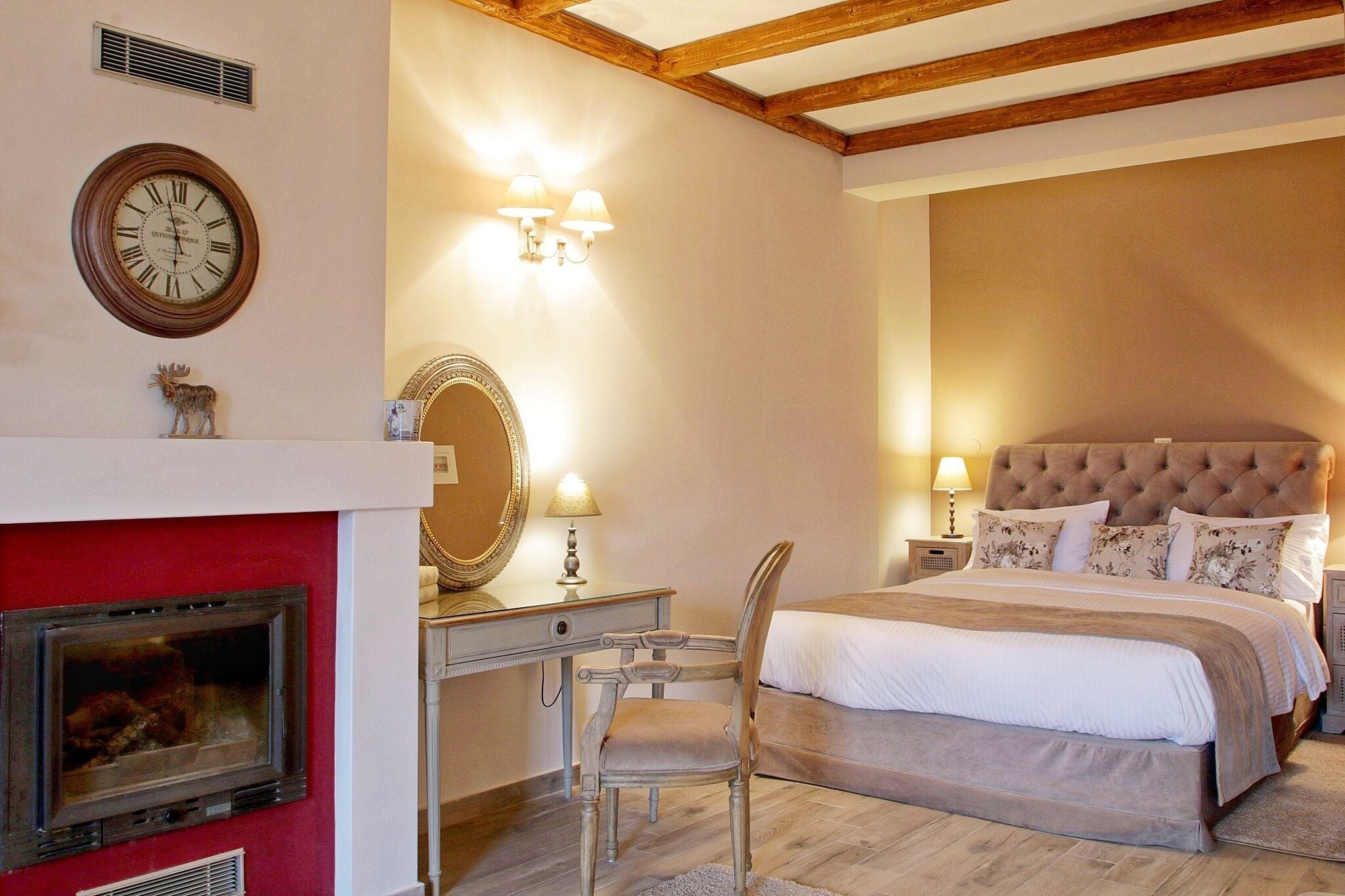 A bedroom with a bed, a desk with a chair, a fireplace, and a wall clock.