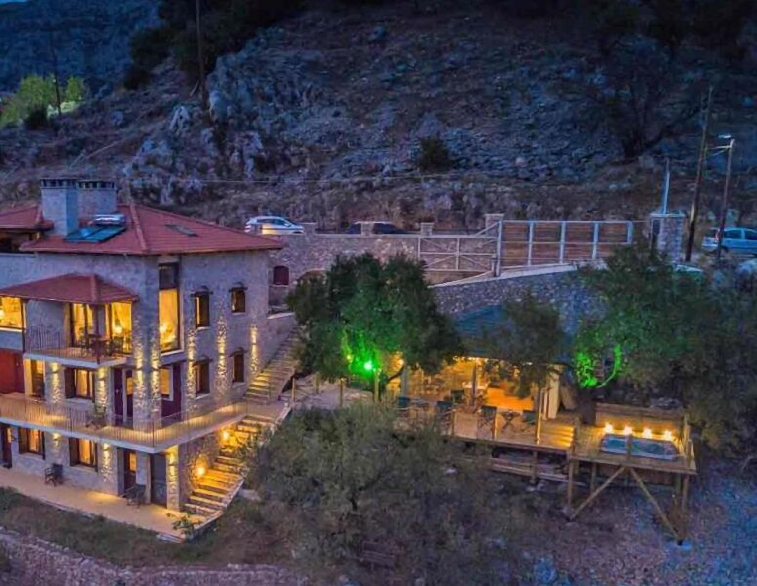 Un bâtiment en pierre avec un toit rouge, un balcon et une terrasse en bois agrémentée de lumières.