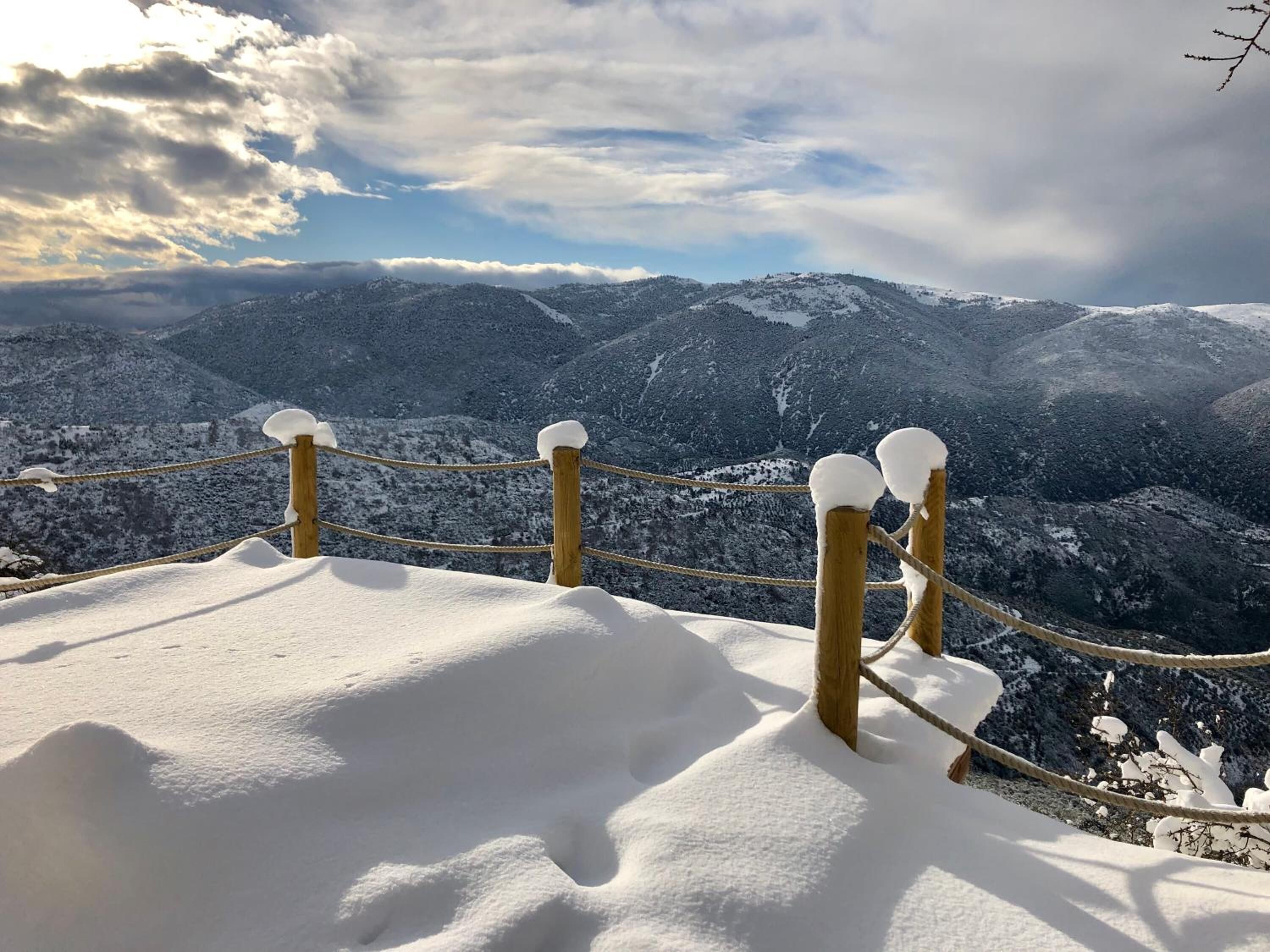 Un paysage montagneux enneigé, avec une barrière faite de cordes et des poteaux en bois.